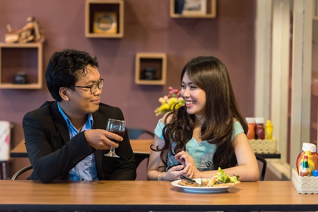 Couples on a date in an eatery, toasting to a wine while smiling to themselves.